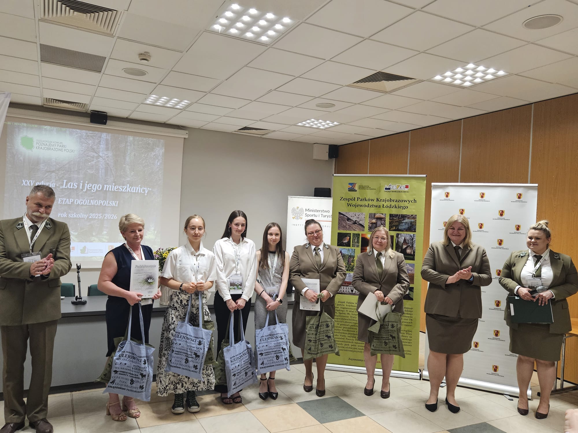 9nsoób pozuje do zdjęcia z dyplomami i nagrodami. 5 osób w mundurach - przedsatawiciele Parków Krajobrazowych. 4 osoby - drużyna reprezentująca województwo śląskie