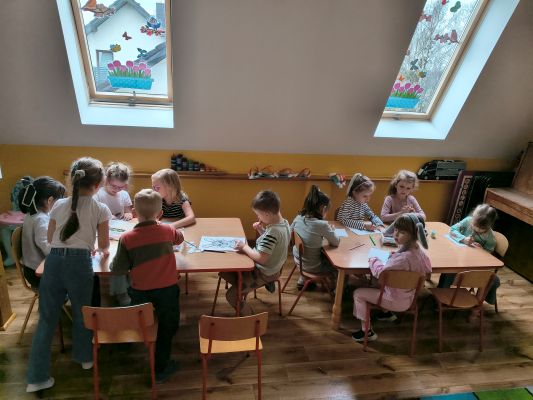 Przedszkolaki siedzą przy stolikach i kolorują świąteczne obrazki.